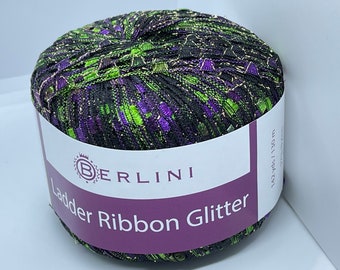 Op de afbeelding: Een bol zwart, groen en paars garen met gouden glitter. Het garen is gelabeld "BERLINI Ladder Ribbon Glitter".