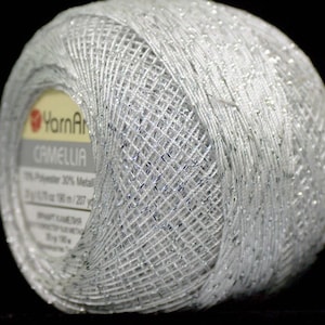 Puede incluir: Una madeja de hilo metálico plateado con una etiqueta que dice "YarnArt Camelia 70% Poliéster 30% Metálico 100g/125m - 136 yds/137 yds"