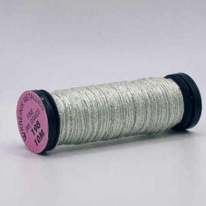 May include: A spool of Kreinik metallic fine (#8) braid thread in a shimmering light silver color. The spool features a pink circular label on the end with the text Kreinik Metallics, Fine (#8) Braid, 198, and 10M printed in black ink.