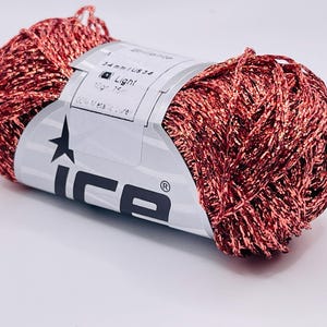 May include: A spool of red and gold metallic yarn. The label reads "Brilliance", "Light", and "10gr 75m". The brand name "ice" is printed on the label. The yarn is a light, shiny material.
