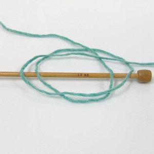 May include: A skein of light blue yarn wrapped around a wooden knitting needle with a 3.0 mm marking.