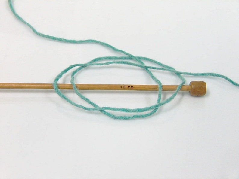 May include: A skein of light blue yarn wrapped around a wooden knitting needle with a 3.0 mm marking.