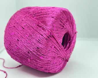 Può includere: Un gomitolo di filato fucsia vibrante con paillettes incorporate. Il filato è avvolto strettamente, creando una superficie strutturata. Le paillettes sono sparse sulla superficie, aggiungendo un tocco di brillantezza. Ideale per progetti di maglia e uncinetto.
