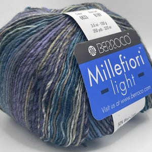 May include: A skein of Berroco Millefiori Light yarn in colourway 6833, 8189. The yarn is a blend of wool and nylon and is 100 grams and 320 metres long. The yarn is a variegated colour with shades of blue, purple, and green.