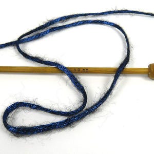 May include: A skein of blue yarn with a metallic sheen wrapped around a wooden knitting needle. The needle is labeled "5.0 mm".