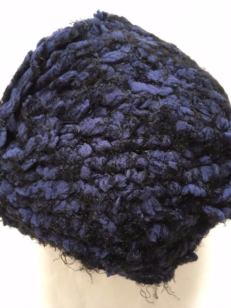 May include: A close-up of a blue and black yarn ball. The yarn is textured and fluffy.