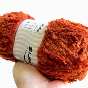 Op de afbeelding: Een bol oranje pluche garen met een wit label waarop "Panda" en "SULERS" staat.