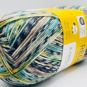 May include: A skein of variegated yarn featuring a blend of blue, green, yellow, and beige fibers. A yellow paper label wraps around the center, displaying the text 100 g = 420 m, 3.5 oz = 459 yds, Oeko-Tex, and Regia 4-fädig.