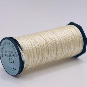 May include: A spool of off-white metallic thread wrapped around a black plastic core. The label on the end reads Kreinik Metallics, Medium (#16) Braid, 191, and 10M. The thread has a shimmering, reflective quality and is wound tightly.