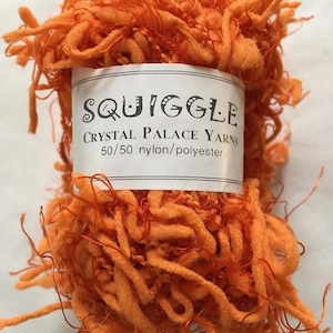 Puede incluir: Un ovillo de hilo naranja llamado "Squiggle" de Crystal Palace Yarns. El hilo es una mezcla de nylon y poliéster al 50/50.