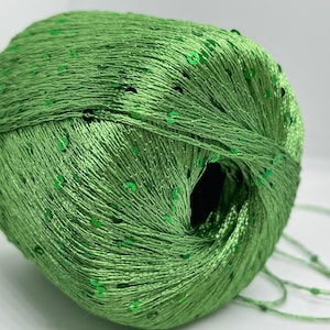 May include: A skein of green yarn with green sequins woven throughout. The yarn is wound into a ball shape.