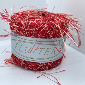 May include: A spool of red and white yarn with a fluffy texture. The label on the spool reads "FLUTTER".