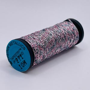 May include: A spool of metallic thread featuring a braided texture with a blend of silver, pink, and dark blue fibers. The blue end cap displays the text KREINIK METALLICS TAPESTRY BRAID #12 271 10M. The thread is wound tightly around a black plastic core.
