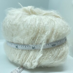 May include: A skein of off-white yarn wrapped around a measuring tape. The tape reads 8, 9, and 10 inches.