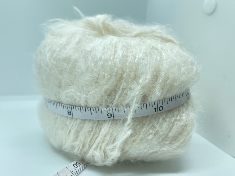 May include: A skein of off-white yarn wrapped around a measuring tape. The tape reads 8, 9, and 10 inches.