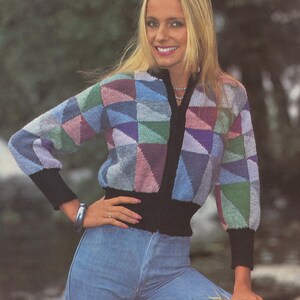 Könnte beinhalten: Ein Strickpullover mit Reißverschluss und einem geometrischen Muster in verschiedenen Farben. Der Pullover hat schwarze Bündchen und einen schwarzen Bund. Das Model trägt eine blaue Jeans.