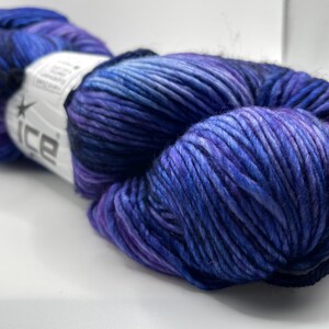 Op de afbeelding: Een bol garen in tinten blauw en paars. Het garen is strak gewikkeld, met zichtbare strengen en een lichte glans. Een wit label met het woord "ice" is zichtbaar.