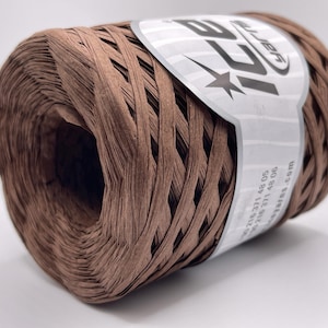May include: A spool of brown raffia yarn. The yarn is tightly wound and has a woven appearance. A white label with black text and a star logo wraps around the spool. The yarn is suitable for crafting and decorative projects.