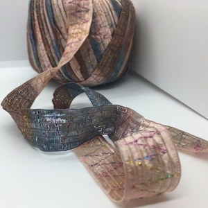 May include: A spool of pink, brown, and blue ribbon with a metallic sheen. The ribbon is woven with a textured pattern and has a subtle shimmer.