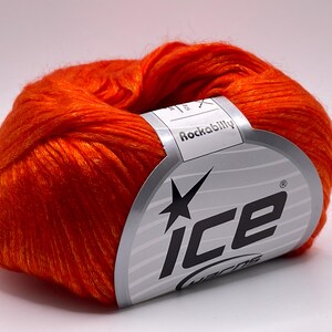 Puede incluir: Ovillo de lana naranja brillante con una etiqueta que dice "Rockabilly" y "ice yarns". La etiqueta tiene un dise&ntilde;o plateado y negro. La lana es de color liso, adecuada para proyectos de punto o ganchillo. La lana es de color naranja brillante.