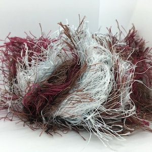 May include: A ball of yarn in shades of brown, white, and burgundy. The yarn is fluffy and has a long, shaggy texture.