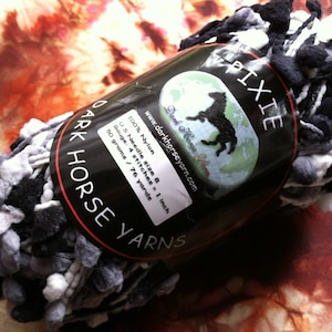 May include: A skein of black, white, and gray yarn called "Pixie" by Dark Horse Yarns. The yarn is 100% nylon and has a gauge of 4 stitches per inch. It weighs 50 grams and is 76 yards long.