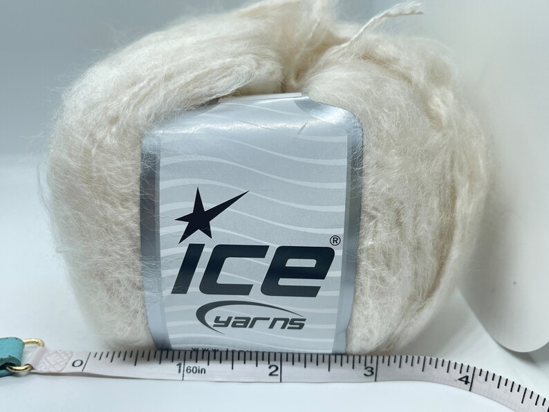 May include: A skein of off-white yarn with a label that says "Ice Yarns" and a star logo. The yarn is about 3 inches in diameter.