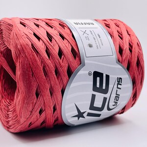 Peut inclure: Une bobine de fil de raphia rouge, idéale pour les projets d'artisanat et de décoration. L'étiquette indique "RAFFIA" et "ICE YARNS". Le fil est 100% viscose et mesure 100 mètres.