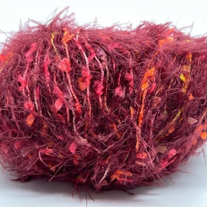 May include: A ball of burgundy yarn with pink, orange, and yellow accents. The yarn has a fuzzy texture and is made of a blend of fibers.