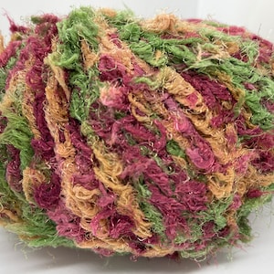 May include: A ball of yarn in shades of green, pink, and beige. The yarn is fluffy and has a slightly sparkly texture.