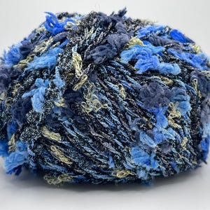 May include: A ball of textured yarn in shades of blue, navy, and cream. The yarn has a fluffy, looped texture with a mix of colors and textures, perfect for knitting or crochet projects.