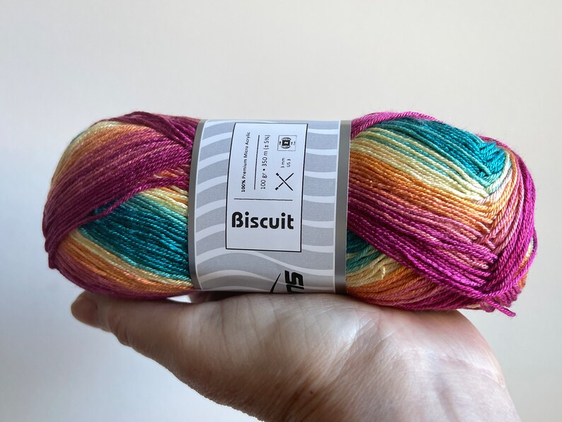 May include: A skein of multi-coloured yarn in shades of pink, orange, yellow, and teal. The yarn is labelled "Biscuit" and is 100% premium acrylic. The label also includes needle size recommendations.