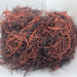 Peut inclure: Un peloton de laine avec un mélange de fibres noires et orange. La laine est très moelleuse et a une texture douce.