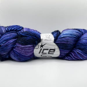 Op de afbeelding: Een streng handgeverfd garen in tinten blauw, paars en zwart. Het garen is gelabeld met "ICE yarns" en lijkt een zacht, getextureerd materiaal te zijn. De kleurveranderingen cre&euml;ren een visueel aantrekkelijk effect.