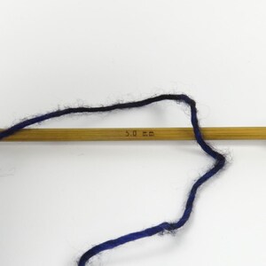 Op de afbeelding: Een houten breinaald met donkerblauw en zwart garen. De naald is gemarkeerd met "5,0 mm". Het garen is over de naald gelust, wat wijst op een breiproject.