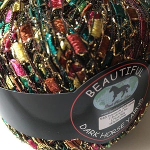 May include: A ball of yarn with a black label that says "BEAUTIFUL DARK HORSE YARNS" and includes details about the yarn, such as the material, weight, and yardage. The yarn is a mix of colors, including gold, red, green, and brown.