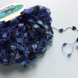 Könnte beinhalten: Ein Knäuel blaues und schwarzes Garn mit einem Etikett, auf dem "NUBS" und "www.debbieblissyarn.com" steht.