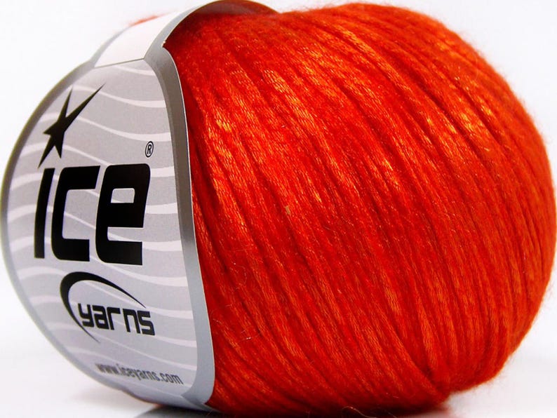 Puede incluir: Una madeja de hilo naranja vibrante, con la marca "ICE YARNS" visible en la etiqueta. El hilo parece suave y texturizado, ideal para proyectos de tejido o ganchillo. La etiqueta es blanca con rayas grises y texto negro.