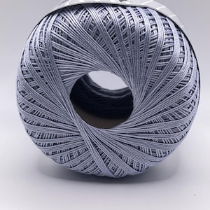 May include: A ball of light blue crochet thread with a central hole. The thread is tightly wound, creating a dense, textured appearance. A label is wrapped around the top of the ball.