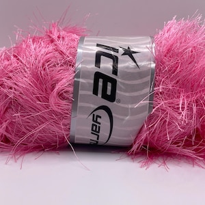 May include: A vibrant pink yarn ball with a fluffy, textured appearance. The yarn is wrapped with a silver label that reads "Ice Yarn" with a star logo. This yarn is suitable for various knitting and crochet projects.