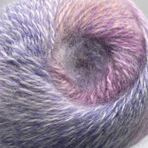 Könnte beinhalten: Nahaufnahme eines Knäuels Garns mit Farbverlauf. Das Garn wechselt von Lavendel- und hellvioletten Farbtönen zu einem tieferen Lila und Rosa. Das Garn hat eine weiche, flauschige Textur.