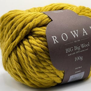 Könnte beinhalten: Ein großer Strang senfgelber Rowan Big Big Wool aus 100 % Merinowolle. Das Etikett trägt die Aufschrift "Rowan" und "Big Big Wool" mit einem Gewicht von 100g. Das Garn ist fest gewickelt und hat ein dickes, strukturiertes Aussehen.