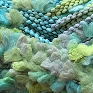 Peut inclure: Gros plan sur un fil doux et moelleux dans des tons de vert, bleu et gris. Le fil est texturé et a un aspect duveteux.