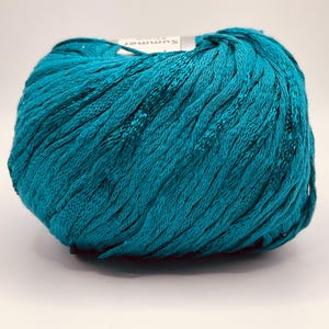May include: A ball of teal-colored yarn. The yarn has a textured, ribbed appearance. A small white label with the word "Summer" is visible on the top of the ball. The yarn is likely used for knitting or crocheting projects.