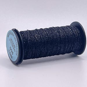 May include: A spool of black metallic thread, specifically Kreinik Medium (#16) Braid, 10m. The thread is wound around a black plastic spool with a light blue circular label on the end featuring the brand name, product type, and length.
