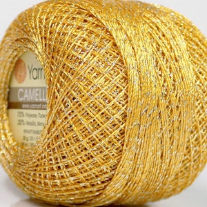 May include: A ball of gold yarn with silver metallic thread. The yarn is labelled "YarnArt Camelia" and has a 70% polyester and 30% metallic composition.