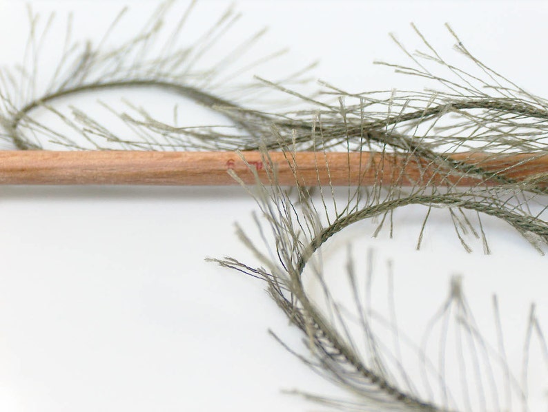 May include: A close-up of a pencil lying on top of two strands of green, string-like material. The material is arranged in a circular shape.