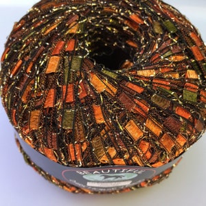 May include: A skein of yarn in a mix of orange, brown, and green colors with gold metallic thread. The yarn is wrapped around a black label with the word "BEAUTIFUL" printed on it.