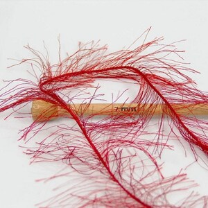 May include: Red feather boa trim with a wooden dowel measuring 7 mm. The boa is made of thin, wispy feathers that create a fluffy, feathery texture.