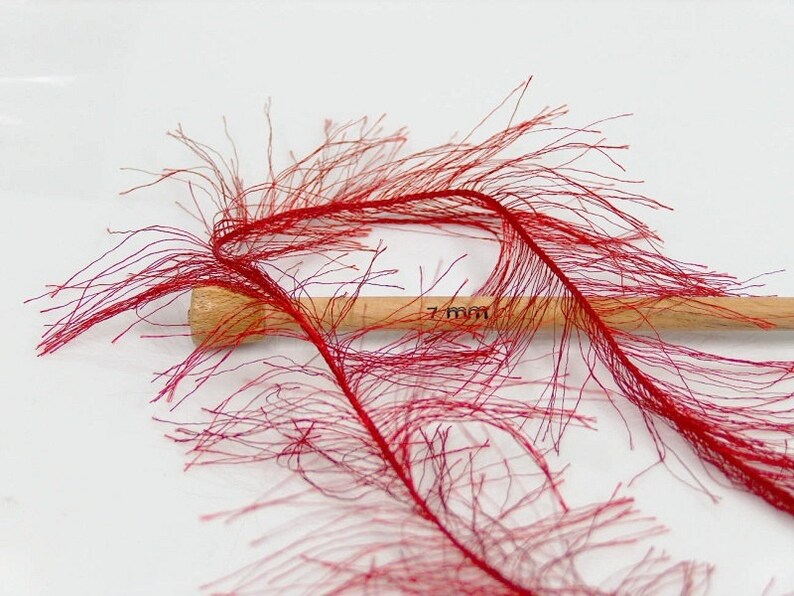 May include: Red feather boa trim with a wooden dowel measuring 7 mm. The boa is made of thin, wispy feathers that create a fluffy, feathery texture.